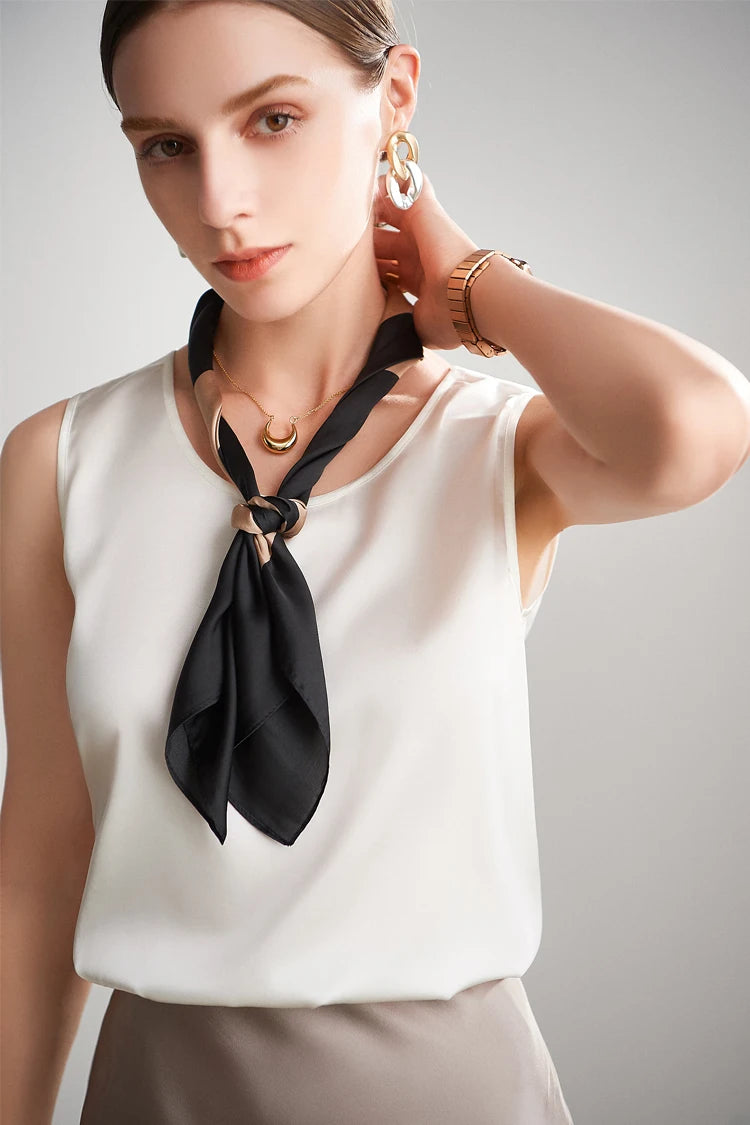 A woman wearing a white sleeveless silk top with a black scarf around her neck against a neutral background