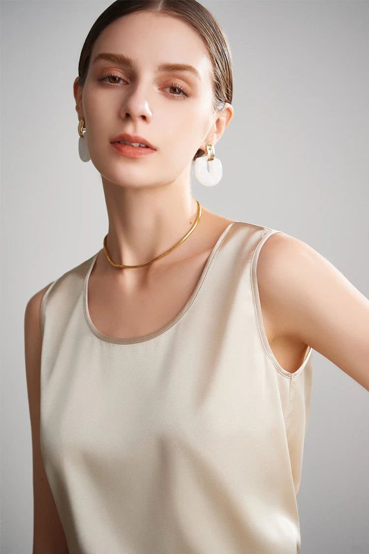 A woman wearing a beige sleeveless silk top with a neutral background
