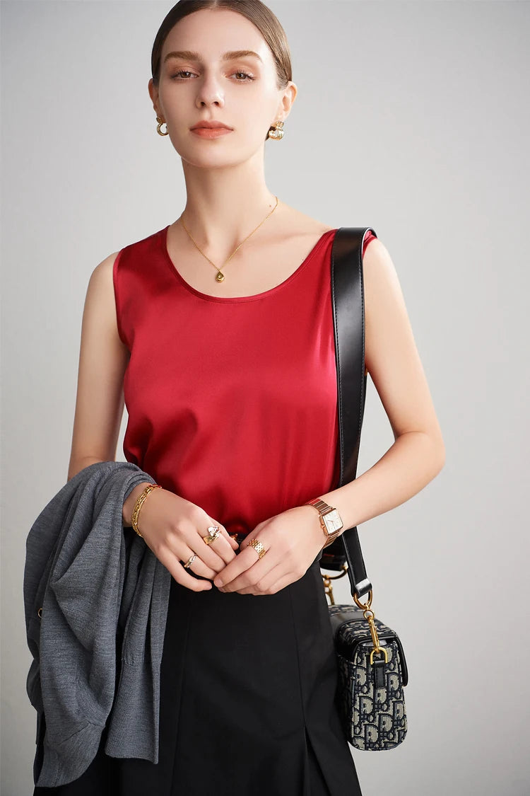 A woman wearing a red top and black skirt with a black handbag on a gray background