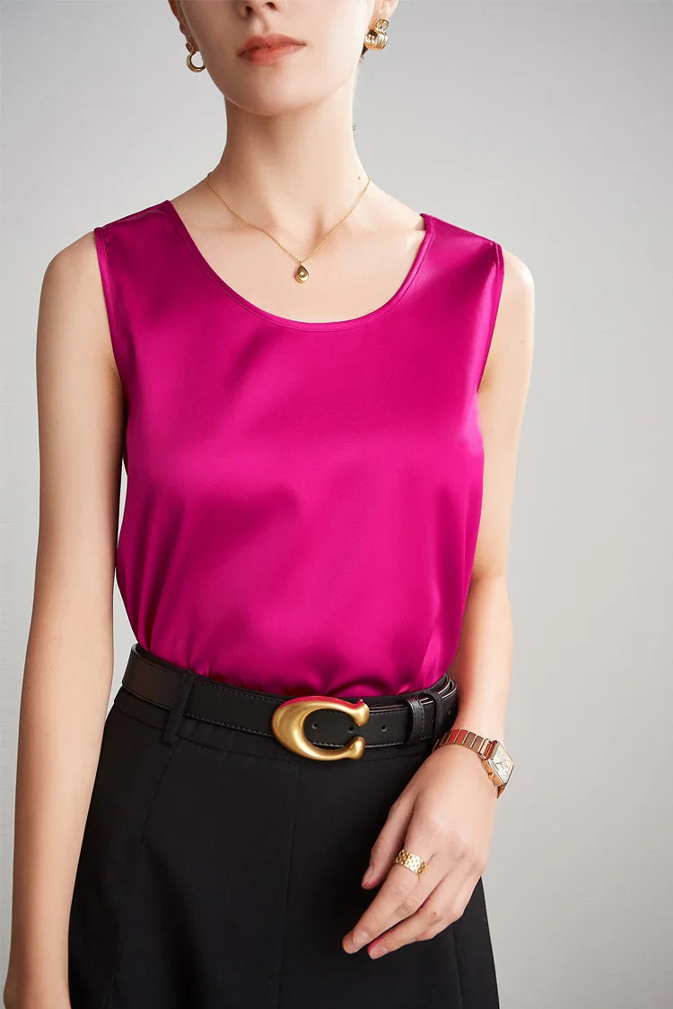 A woman wearing a bright pink sleeveless silk top with black pants on a gray background