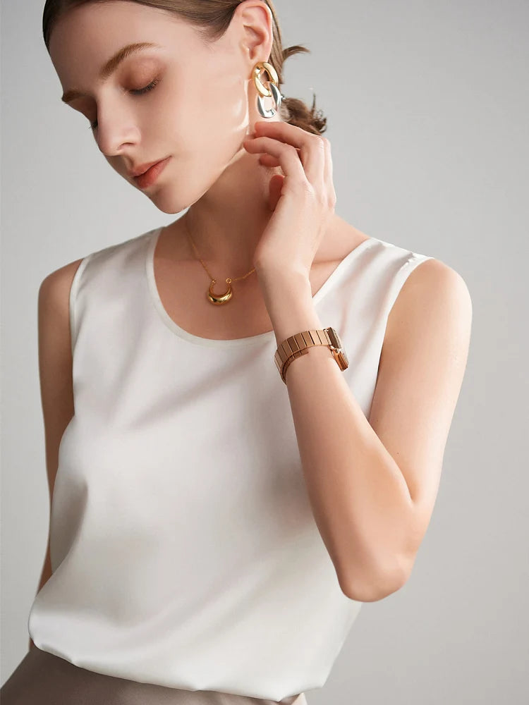 A woman wearing a sleeveless white silk top against a neutral background