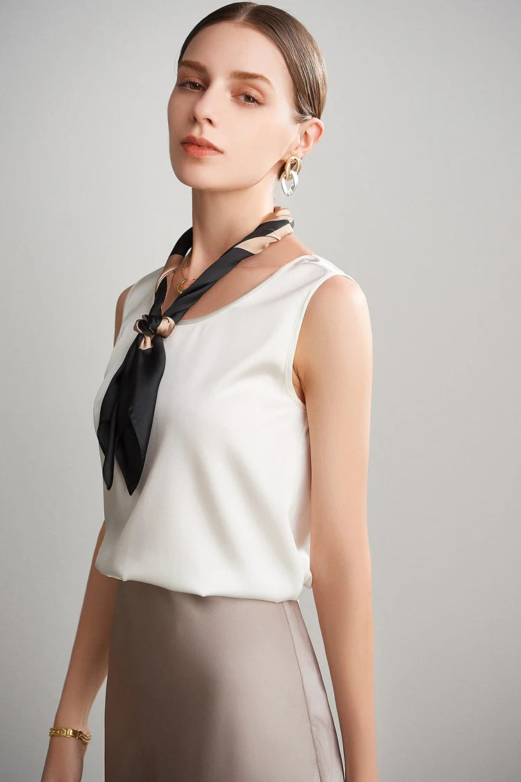 A woman wearing a white sleeveless silk top with a black scarf and gray skirt against a gray background
