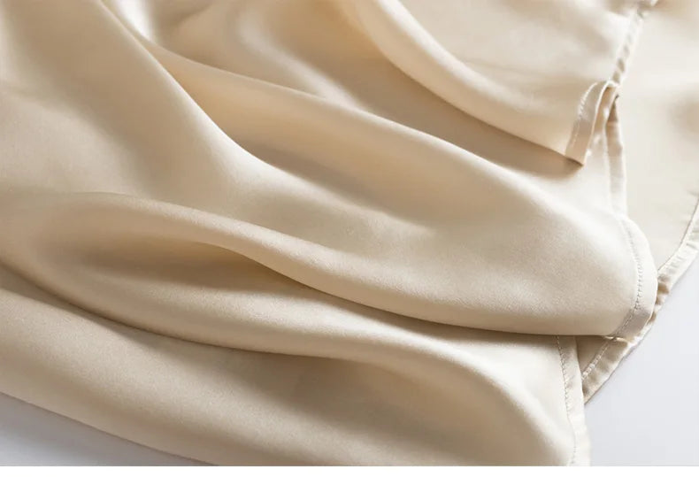 Close-up of a beige sleeveless silk top's hem with a white background