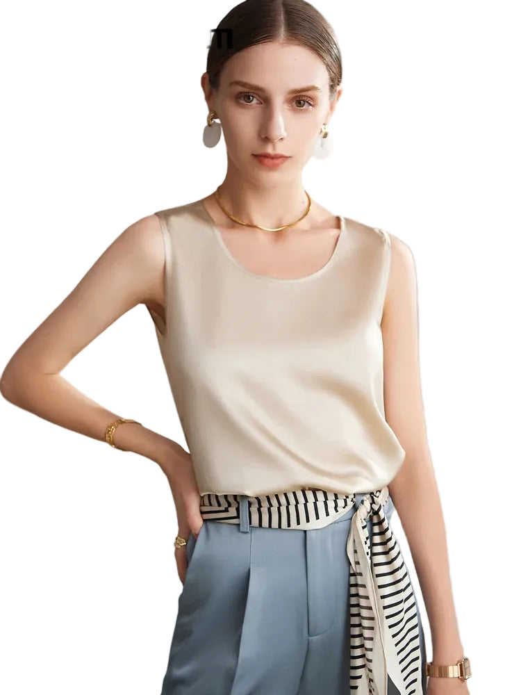 A woman modeling a sleeveless scoop-neck beige silk top, paired with light blue trousers and a black-and-white striped silk tie belt, against a solid white background.